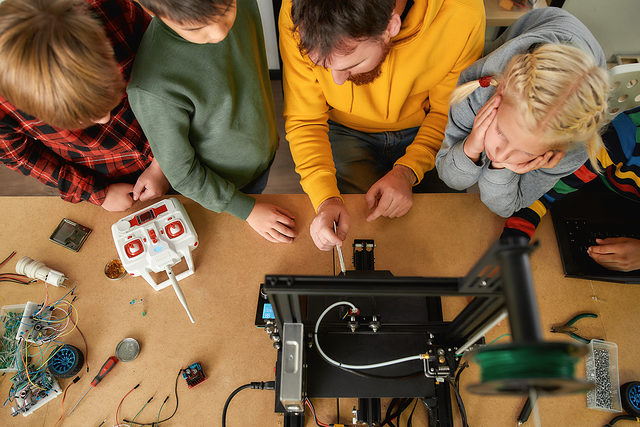 Young male teacher explaining to a group of curious kids working principle of 3d printer at robotics school lesson. Science and education. Top view Schlagwort(e): 3d, printer, electronics, engineering, equipment, innovation, machine, modern, robotics, science, tech, technology, kid, many, school, 3d printer, boy, child, childhood, class, classroom, concept, creative, education, elementary, friends, girl, group, curious, indoors, junior, learning, little, mechanics, person, preteen, print, prototype, prototyping, student, team, teamwork, technical, together, workshop, young, looking, children, teacher, male, 3d, printer, electronics, engineering, equipment, innovation, machine, modern, robotics, science, tech, technology, kid, many, school, 3d printer, boy, child, childhood, class, classroom, concept, creative, education, elementary, friends, girl, group, curious, indoors, junior, learning, little, mechanics, person, preteen, print, prototype, prototyping, student, team, teamwork, technical, together, workshop, young, looking, children, teacher, male
