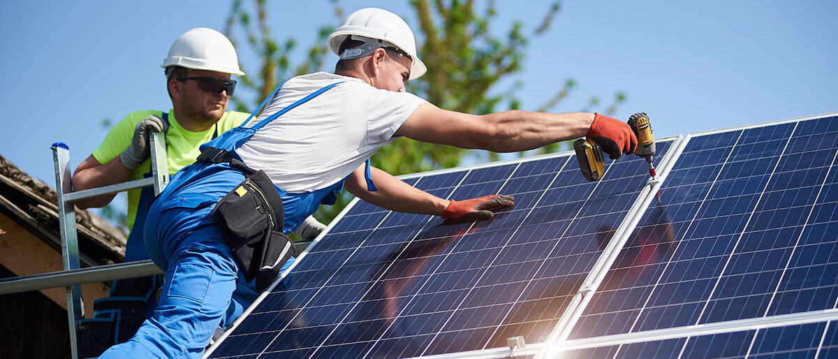 Two workers technicians installing heavy solar photo voltaic panels to high steel platform. Exterior solar system installation, alternative renewable green energy generation concept. Schlagwort(e): system, solar, power, energy, panels, technology, installation, exterior, renewable, alternative, generator, photovoltaic, install, mounting, maintenance, supply, environmental, eco, green, electrical, generation, building, ecological, electric, construction, worker, technician, installer, engineer, professional, men, team, electricity, light, economy, modern, resource, module, background, blue, screwdriver, hight, recycling, structure, cells, texture, price, investment, assemble, eco friendly