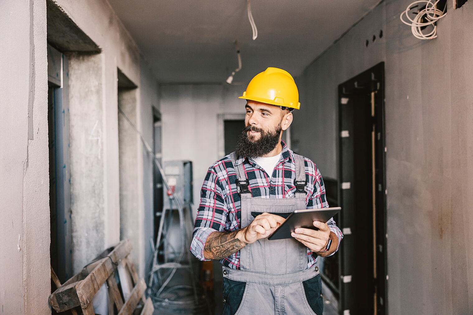 A dedicated worker using tablet for work in a building in a construction process. Schlagwort(e): worker, man, male, guy, people, person, portrait, beard, tattoo, blue collar, repairman, handyman, construction, foreman, job, work, fix, repair, helmet, renovation, site, building, engineer, safety, computer, tablet, construction worker, industrial, construction site, hardhat, coworker, alone, electronic, estate, check, examining, pad, internet