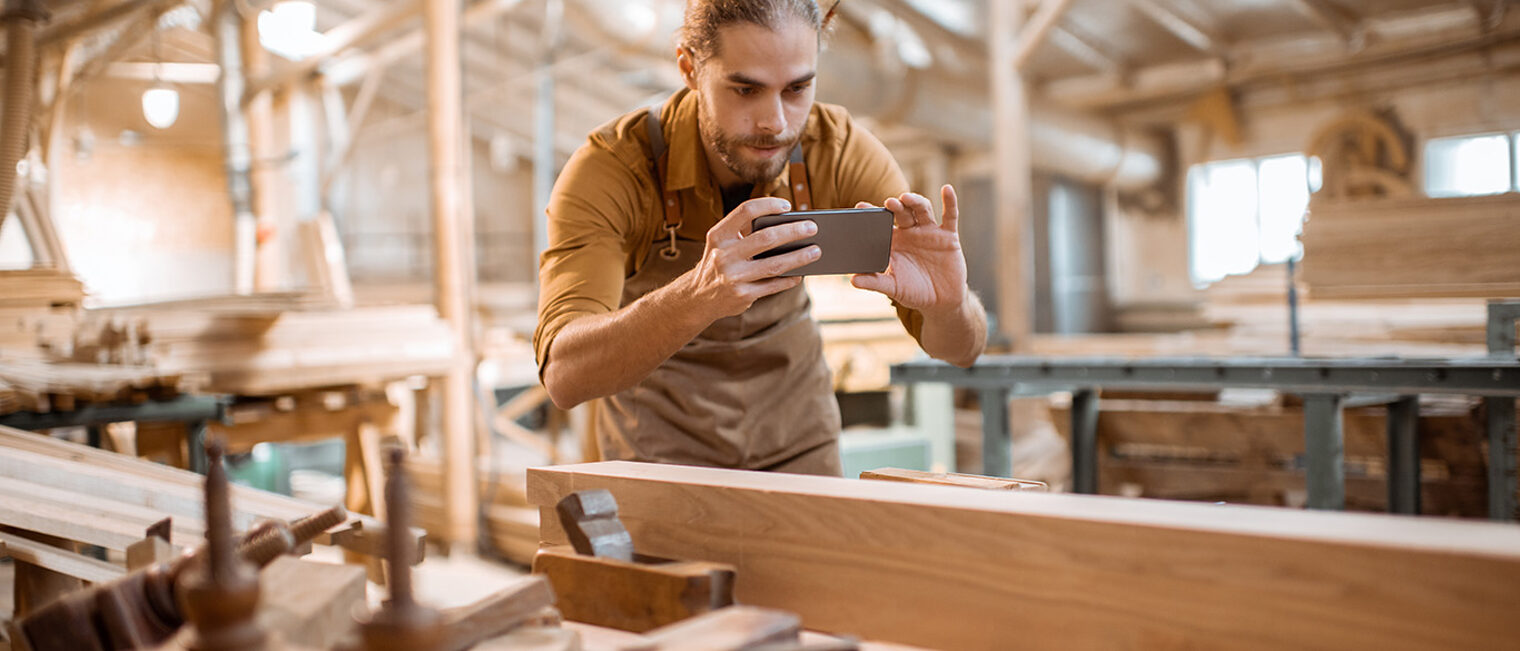 Carpenter photographing with a smart phone his woodwork on the workbench in the joiners shop. Concept of mobile technologies in carpentry Schlagwort(e): carpenter, phone, carpentry, technology, smartphone, worktable, smart phone, craft, wood, tool, picture, hands, craftsman, accuracy, project, expertise, craftsperson, diy, creativity, workbench, photographing, work, crafts, augmented reality, design, woodwork, workshop, worker, manual, interior, furniture, man, timber, designer, joinery, male, occupation, woodshop, caucasian, professional, skill, manufacturing