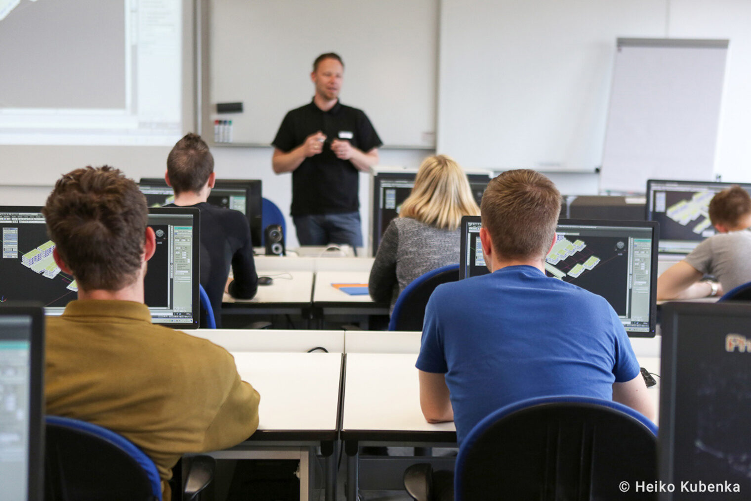 Teilnehmende eines Seminares sitzen in einem EDV Raum und schauen den Dozenten an Auszubildende nehmen an einem Seminar teil und sitzen in einem EDV Raum